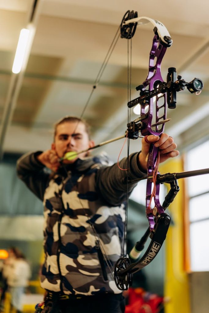 A man intensely focuses on aiming a purple compound bow at an indoor archery range.